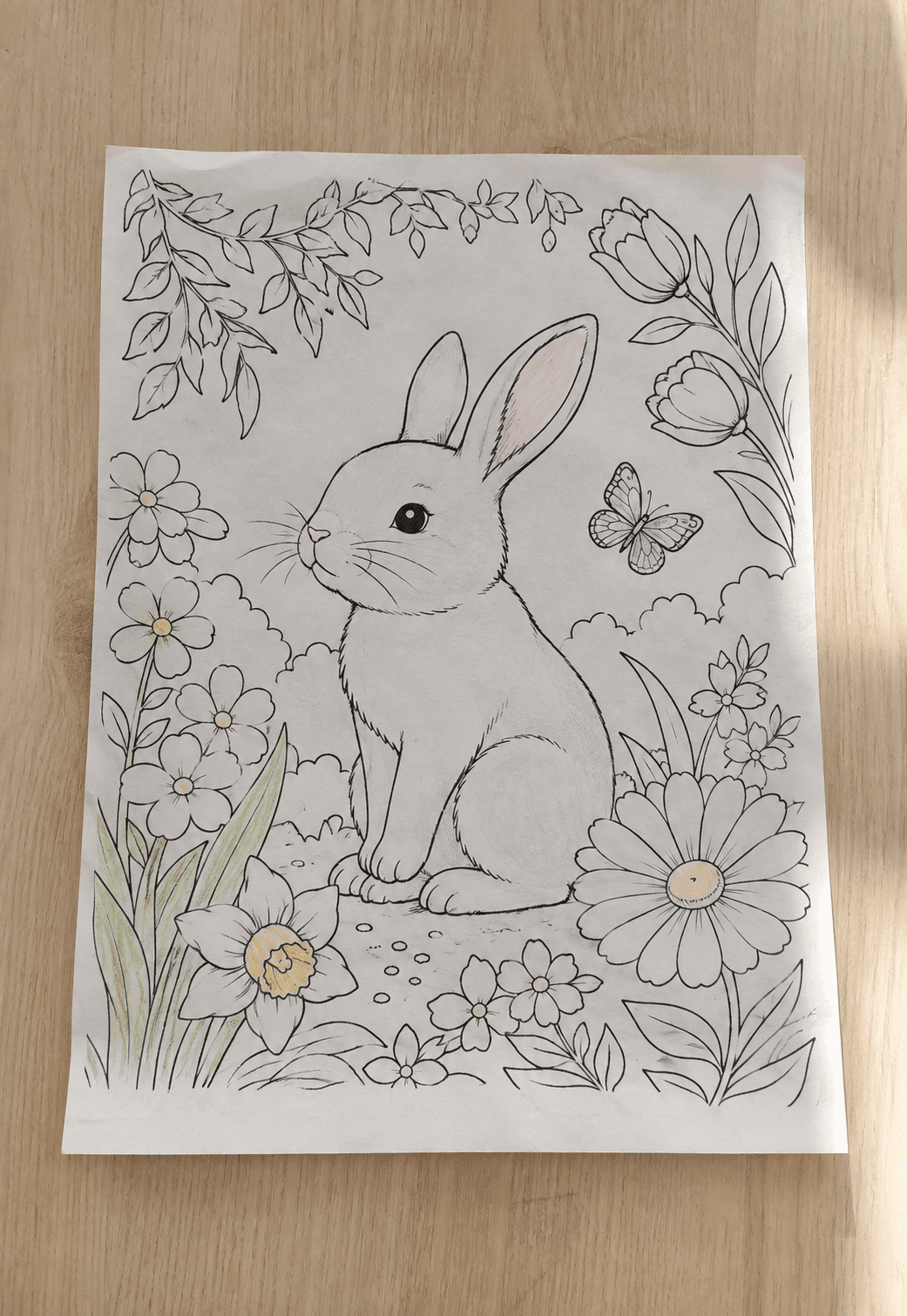 Photographed original rabbit-and-flower coloring page lying flat on a wood table with faint pencil marks